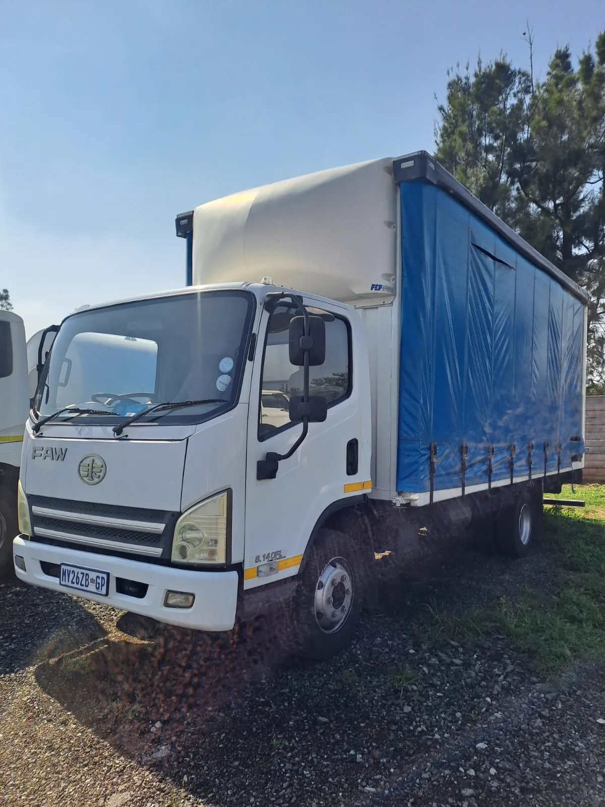 White FAW curtain-side truck with a blue curtain parked in a yard